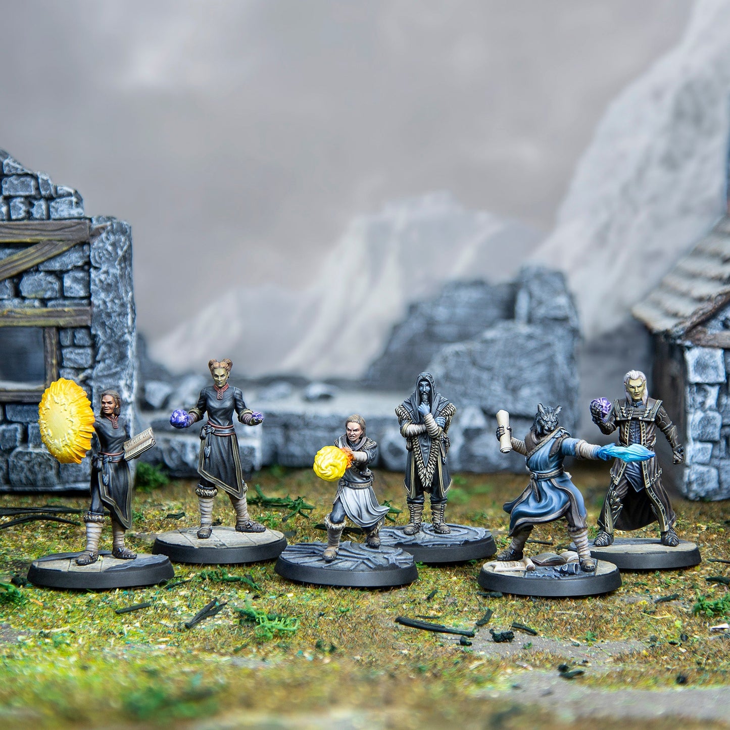 Tabletop diorama: Six fantasy spellcaster miniatures in action amidst ruined buildings and mountains
