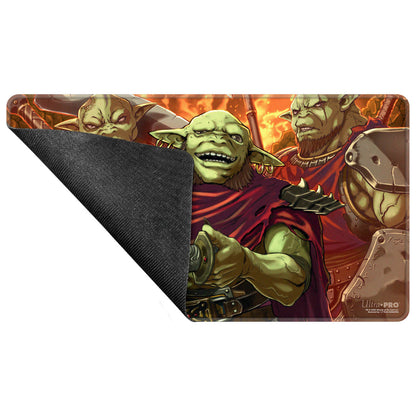Playmat: Grinning green goblin in red cloak holds sword hilt, flanked by two orcs on fiery background. Mat corner peeled back
