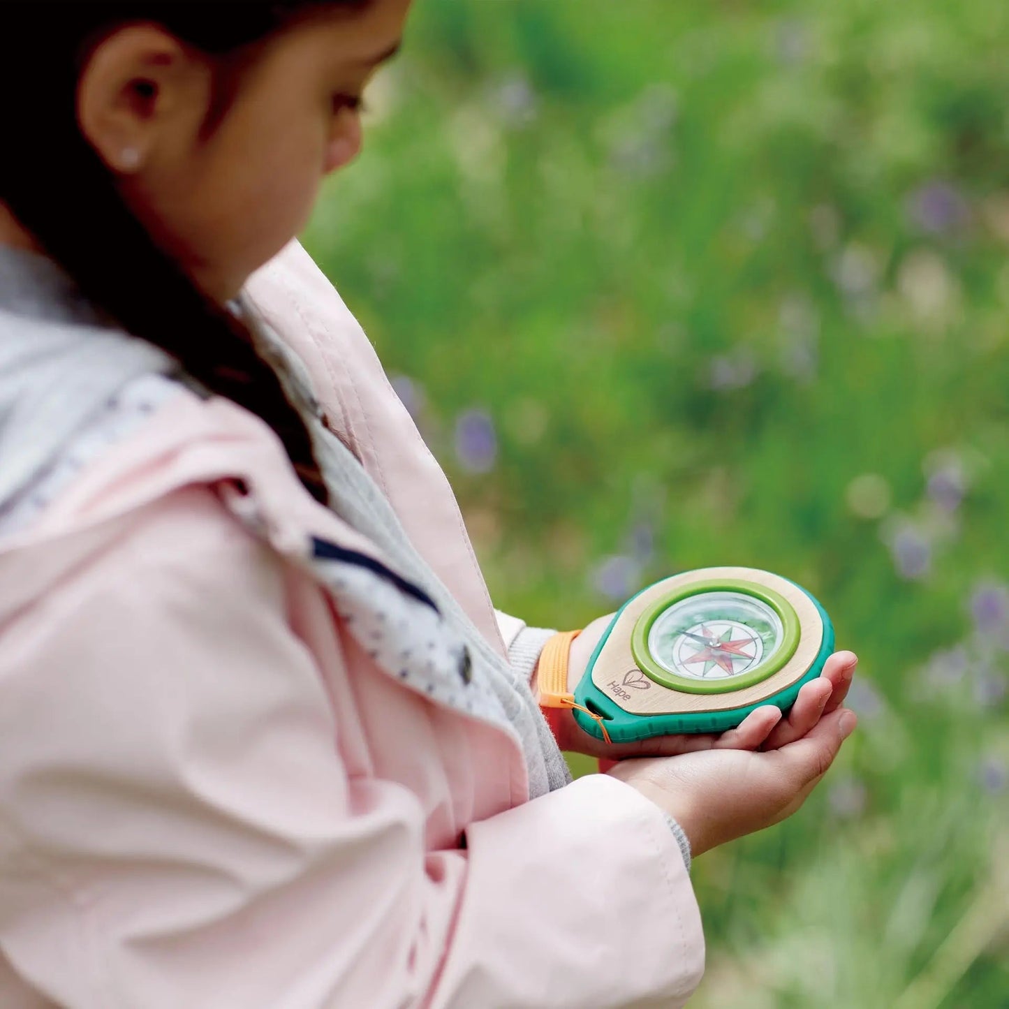 Child in a pink jacket closely examines a wooden toy compass held in her hands outdoors