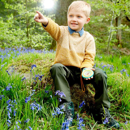 Boy sits in a bluebell forest, holding a compass and pointing ahead excitedly