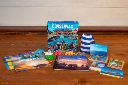 The Conservas board game box, cards, tokens, rulebooks, and a striped bag are spread out on a wooden surface