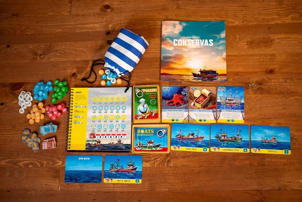 The Conservas board game, with its box, rulebook, cards, tokens, and a striped bag, is laid out on a wooden table