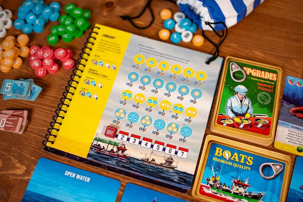 Conservas board game components spread across a wooden table, featuring a spiral-bound booklet, stacks of game cards, and numerous colorful tokens