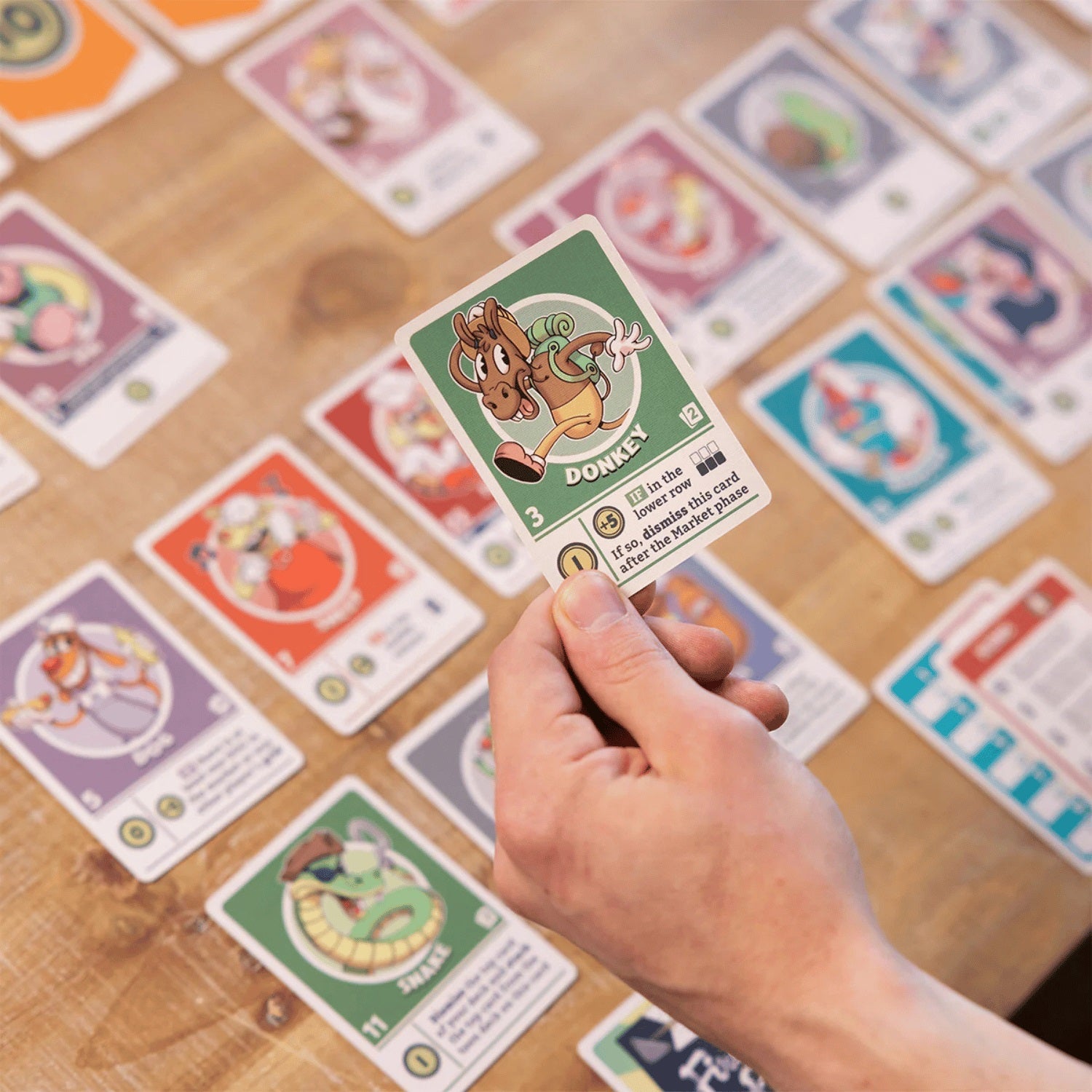 Hand holding a green character card labeled "Donkey" over a table covered in colorful trading or board game cards