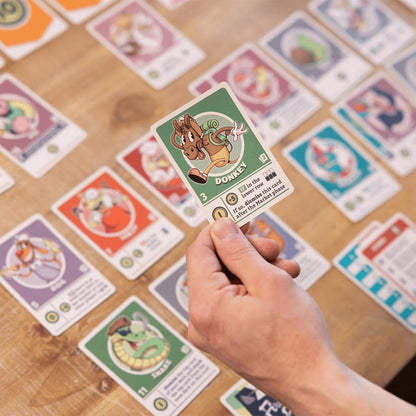 Hand holding a green character card labeled "Donkey" over a table covered in colorful trading or board game cards