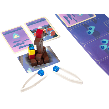 Tweezers holding blue cubes near a stacked tower of colorful wooden blocks and game cards
