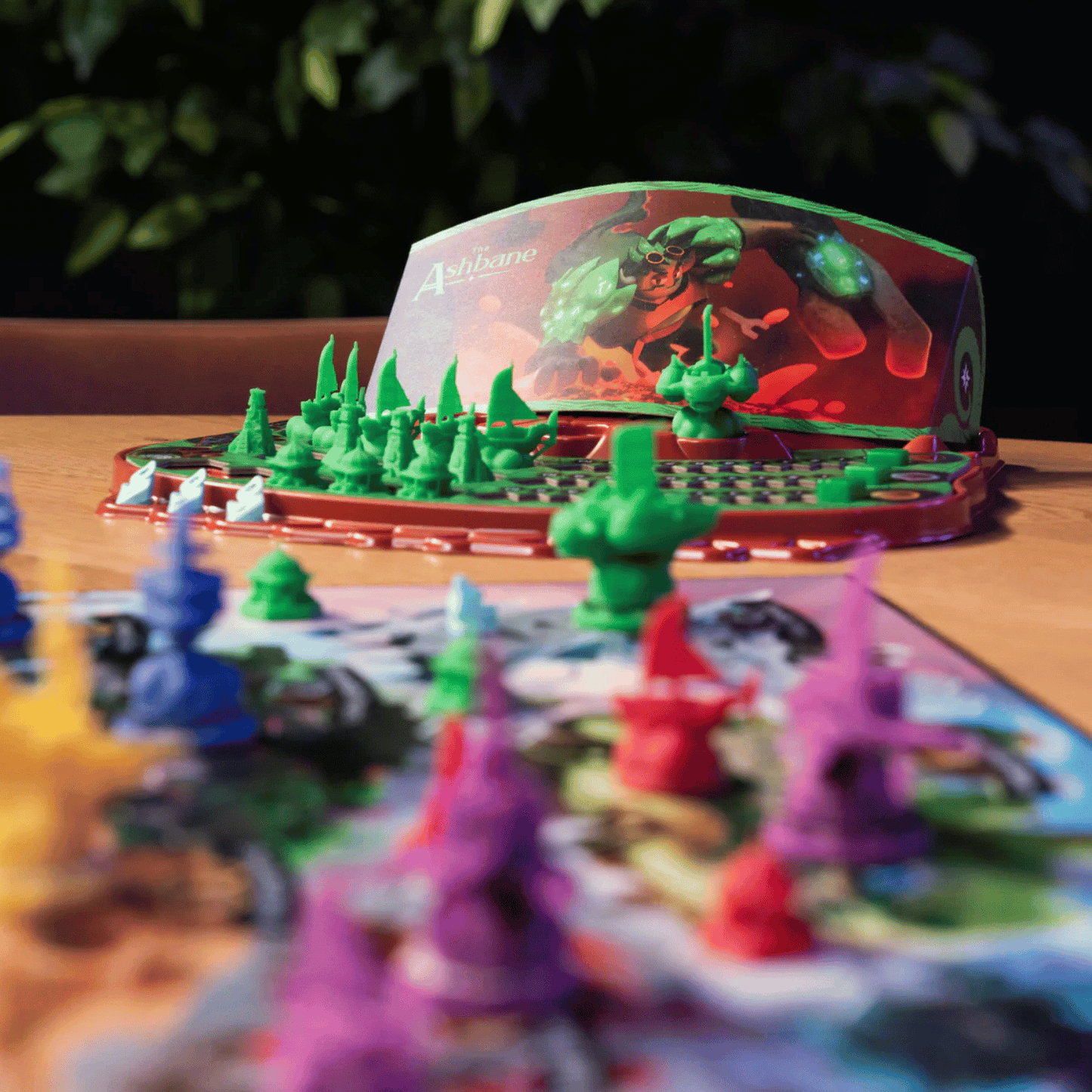 Close-up of "The Ashbane" board game, showing green fortress miniatures and colourful plastic pieces on a wooden table