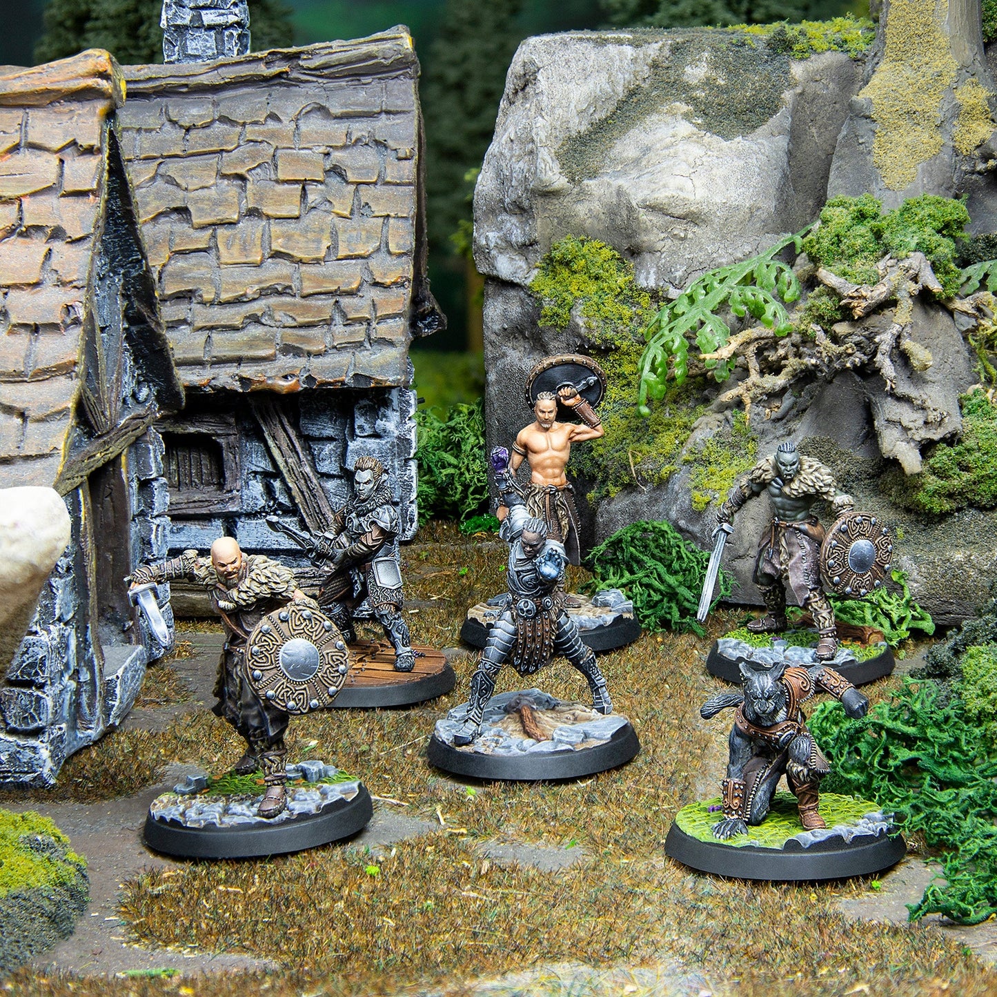 Fantasy tabletop skirmish with six diverse miniatures in combat poses on a diorama featuring a hut and rocks