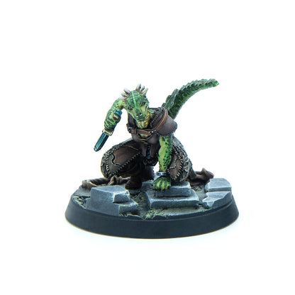 Green scaled lizardfolk miniature in leather armor, crouching with a dagger on a stone base