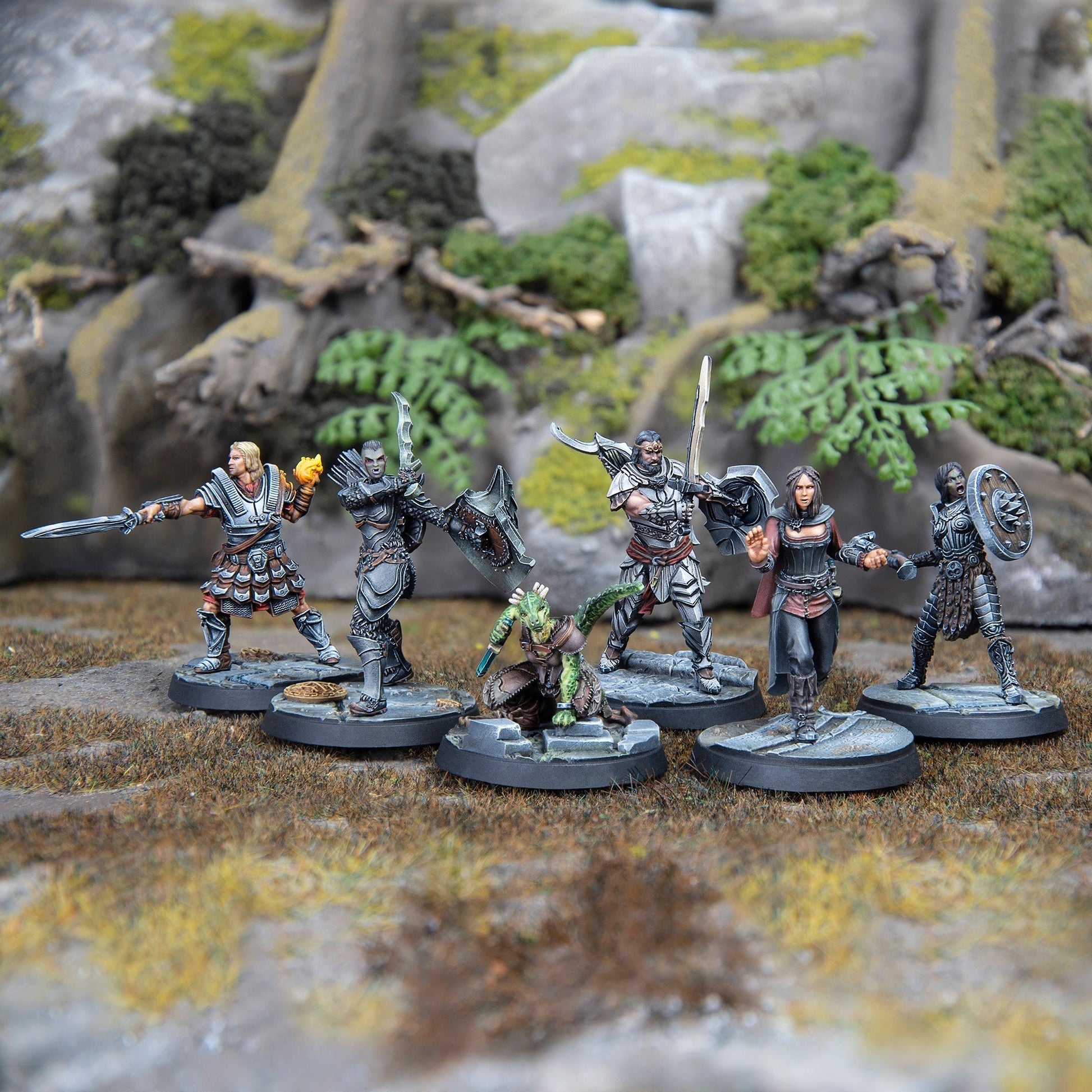 Six fantasy war-game miniatures, including warriors and a lizard-folk, posed on a rocky, mossy terrain