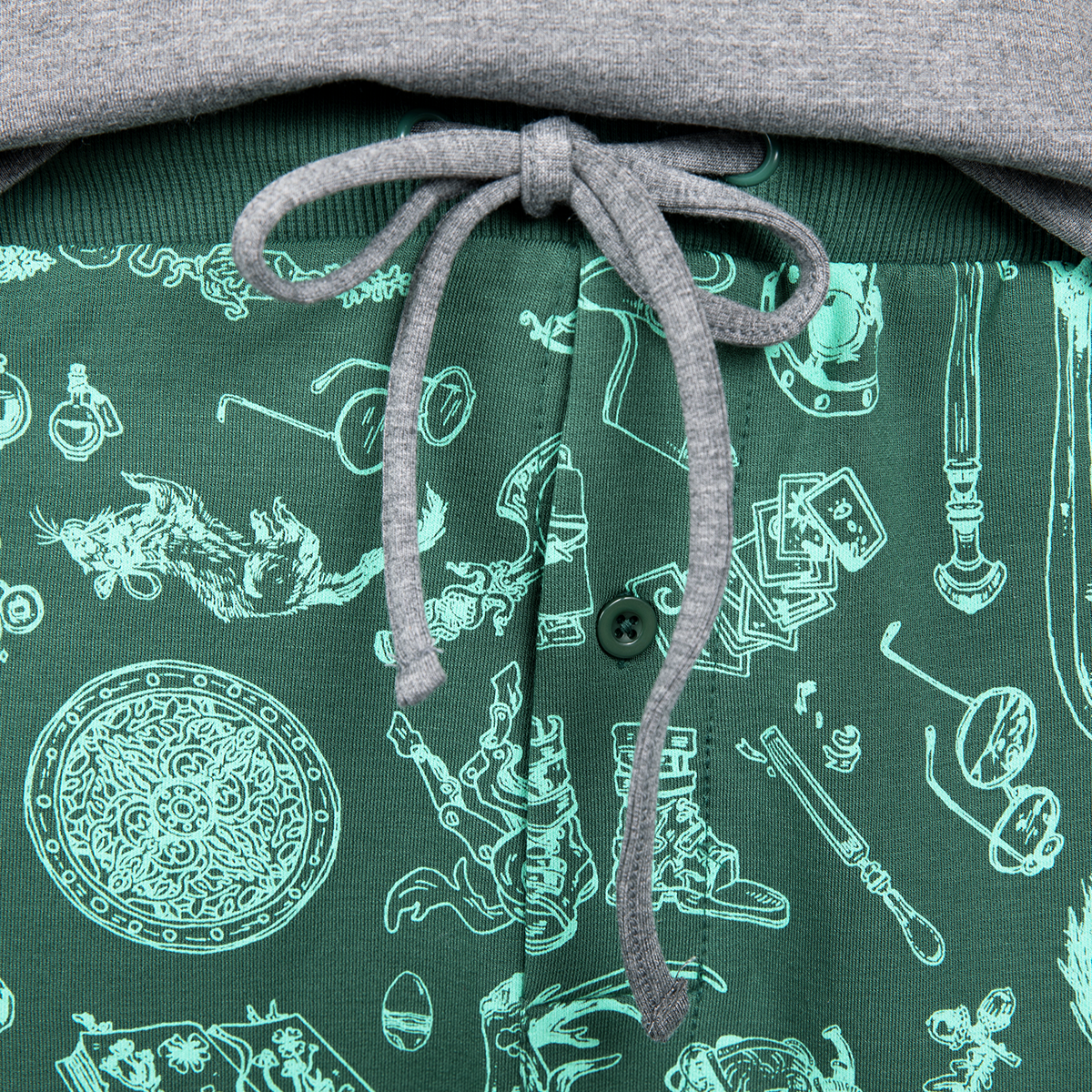 Close-up of a green garment with teal fantasy-themed illustrations, a grey drawstring bow, and a button