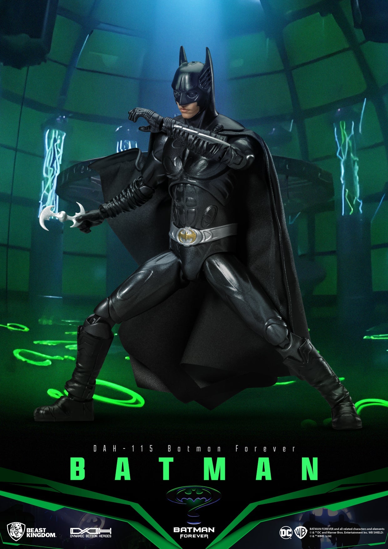 Val Kilmer as Batman from the 1995 film Batman Forever in a black suit with silver belt holding a batarang in a dark green room