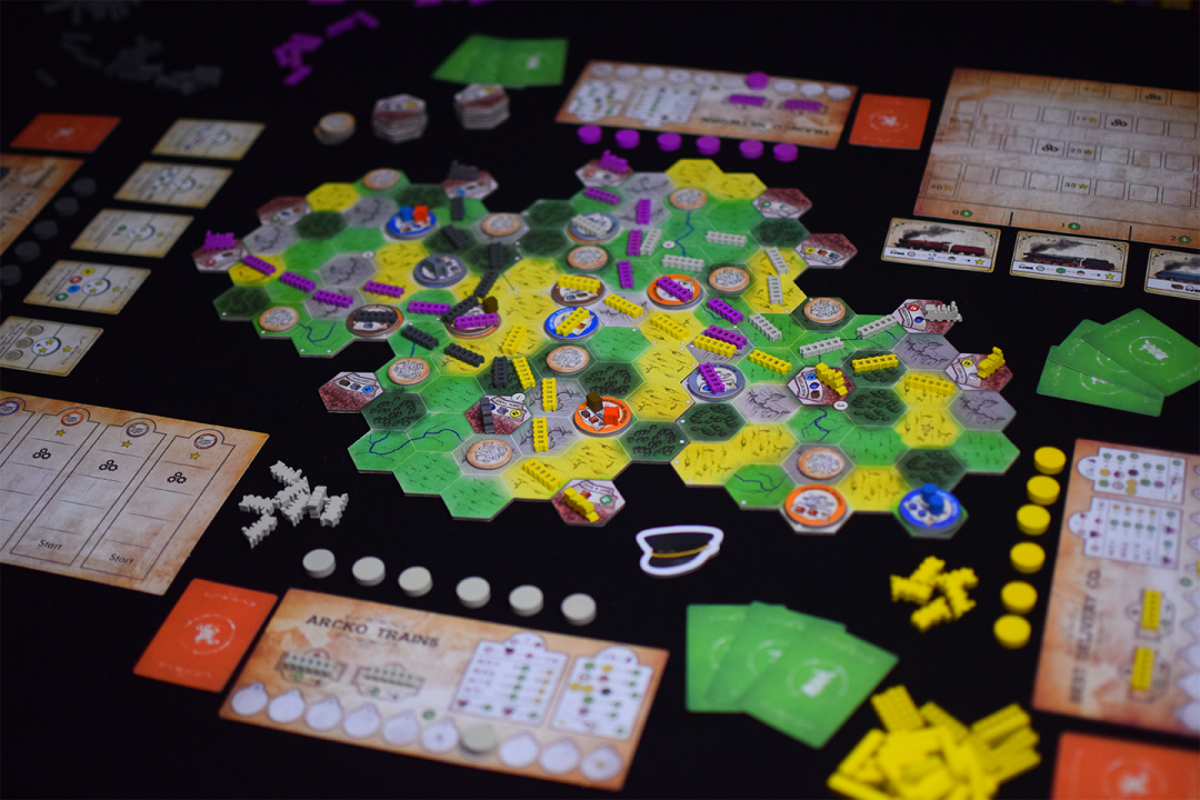 A vibrant Small Railroad Empires board game in play, featuring a hexagonal map with colorful pieces, cards, and tokens