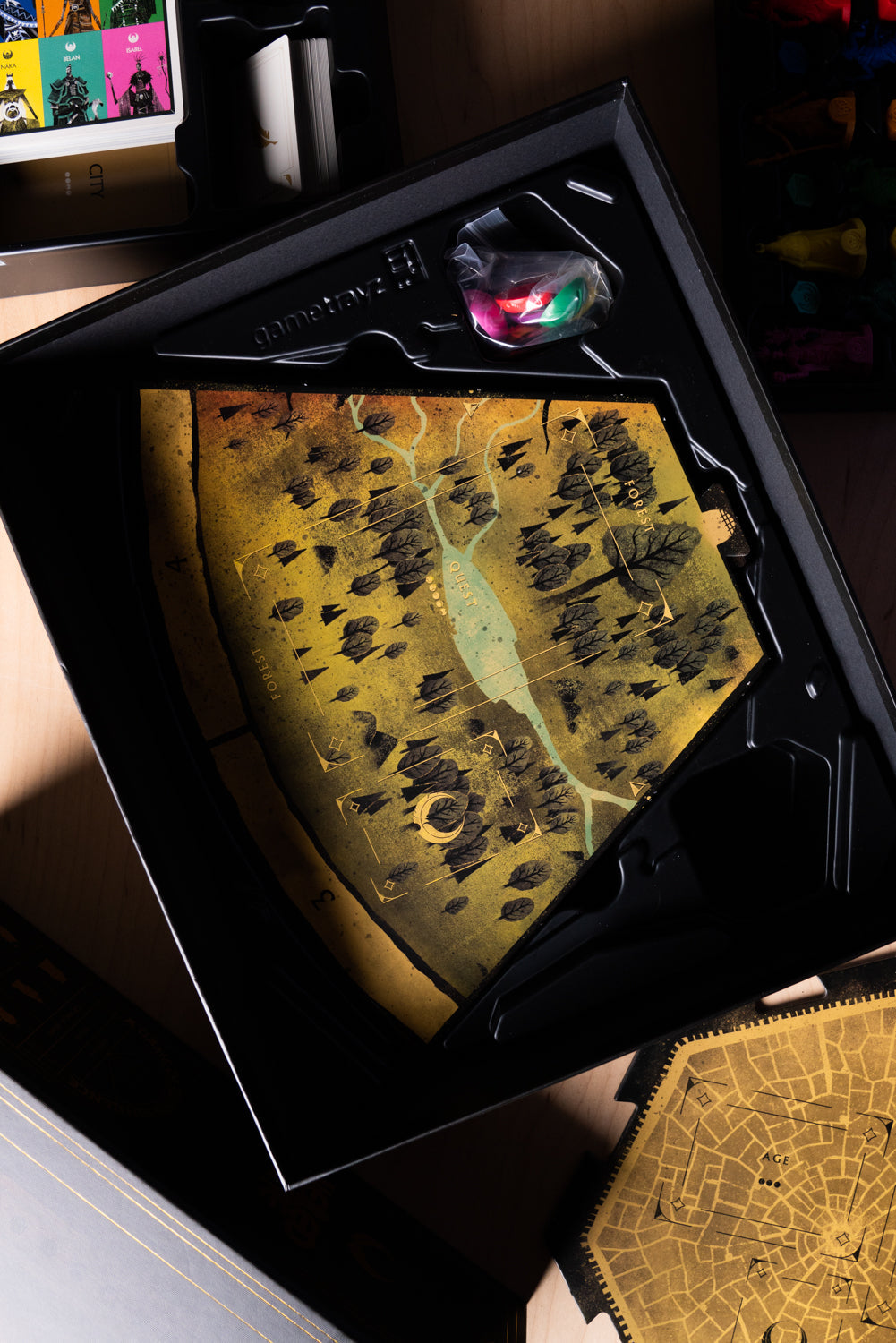 Game box insert with a large, gold and black forest map tile, character cards and tokens