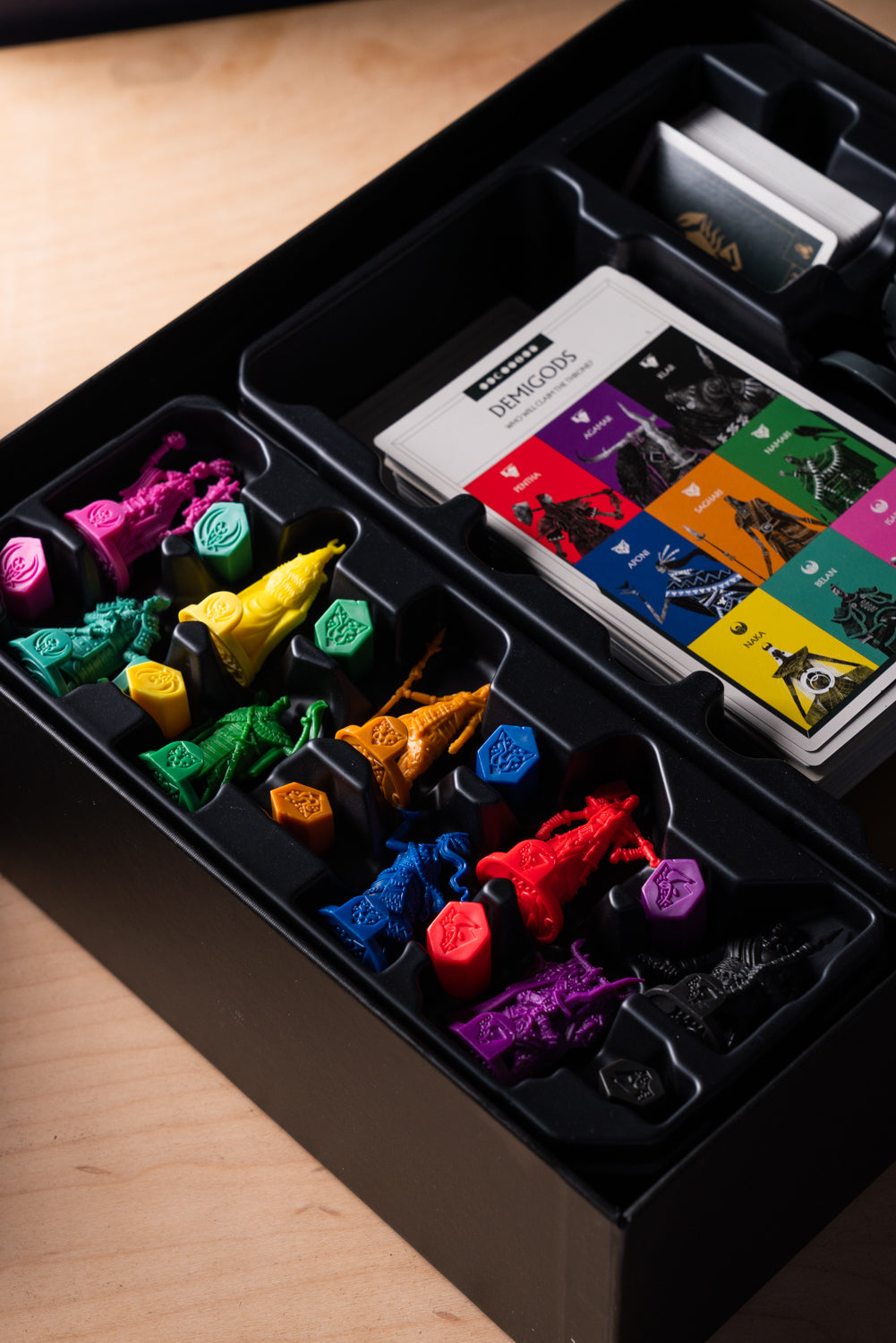 Close-up of a board game box containing organized, multicoloured plastic miniatures and Demigods character cards