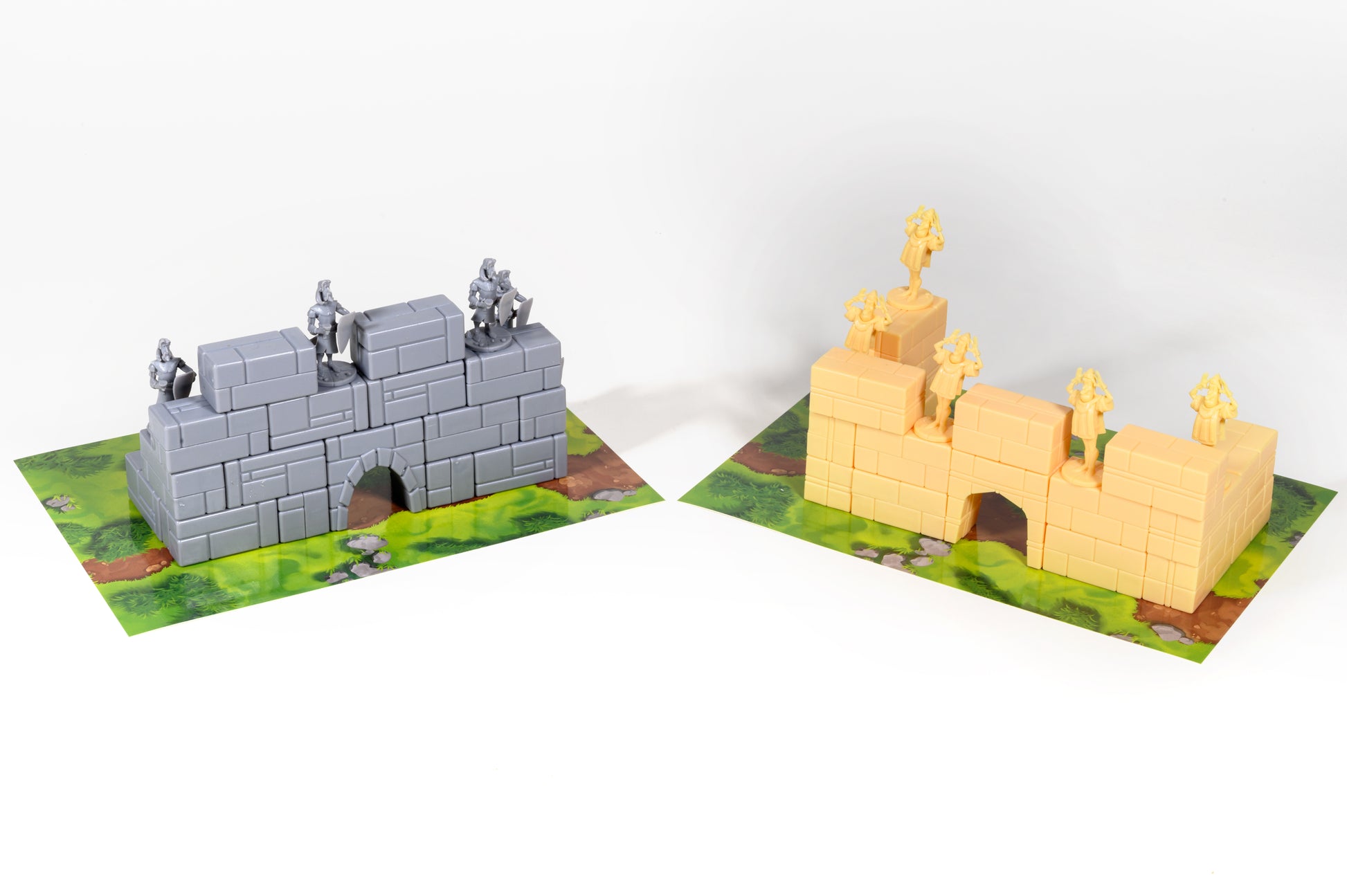 Two tabletop game models: a grey castle wall with knights and a yellow wall with figures, on green terrain mats