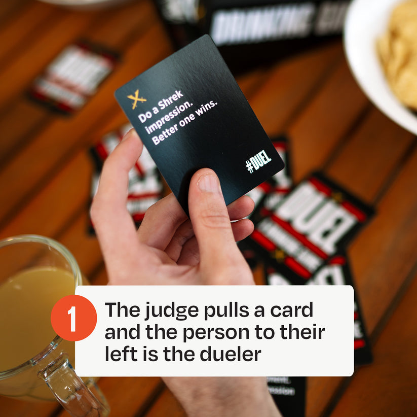 A hand holds a black &quot;Duel&quot; game card instructing &quot;Do a Shrek impression. Better one wins.&quot;
