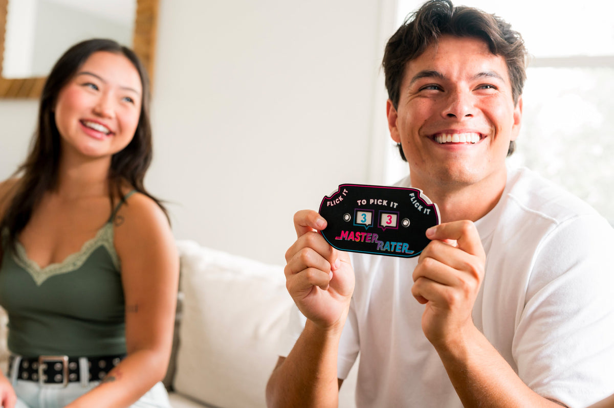 Smiling man holds up a black Master Rater game card with blue and pink numbers