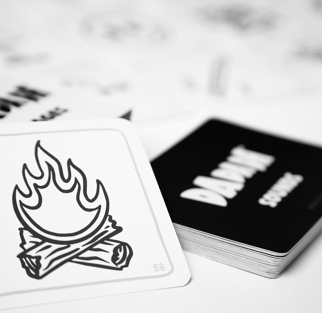Black and white playing card with a campfire icon, next to a stack of black game cards labeled 'DANGEROUS'
