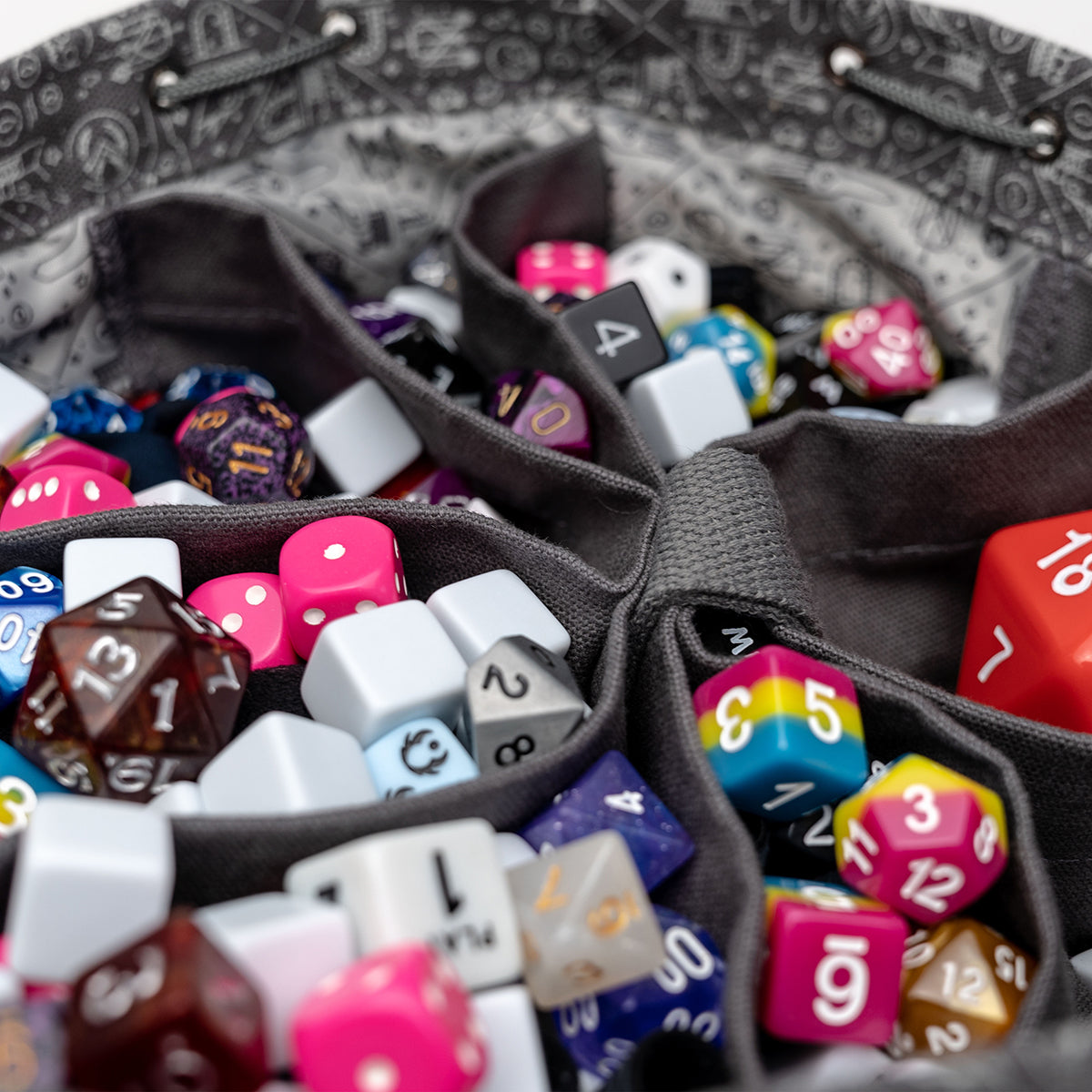 Colorful polyhedral gaming dice are organized in the compartments of a grey fabric storage bag