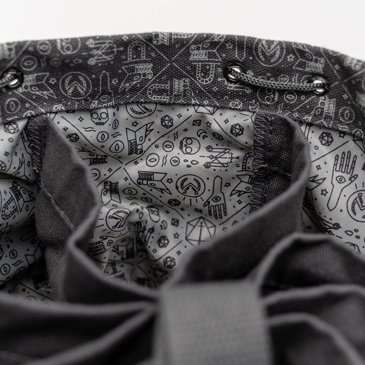 Close-up of an open dark grey drawstring bag's interior, showing a light grey lining with D&D-themed patterns