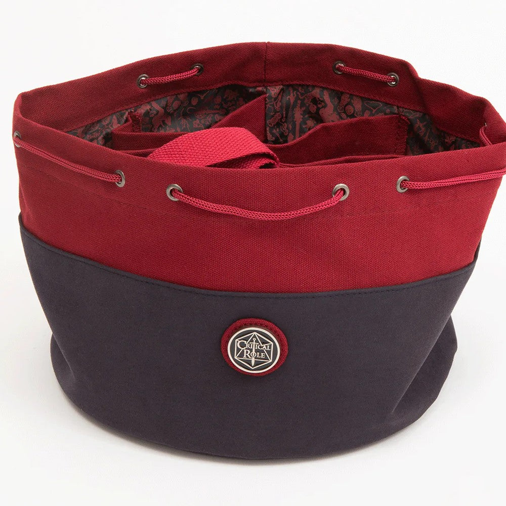 A two-tone red and navy Critical Role Bailey's drawstring bag, open to reveal internal compartments and a logo badge