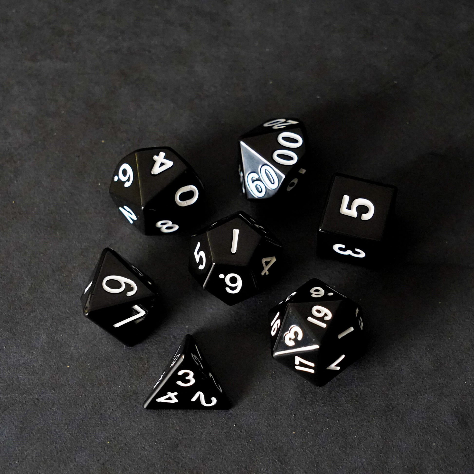 Full black metal polyhedral dice set fanned out on dark background premium RPG tabletop gaming dice