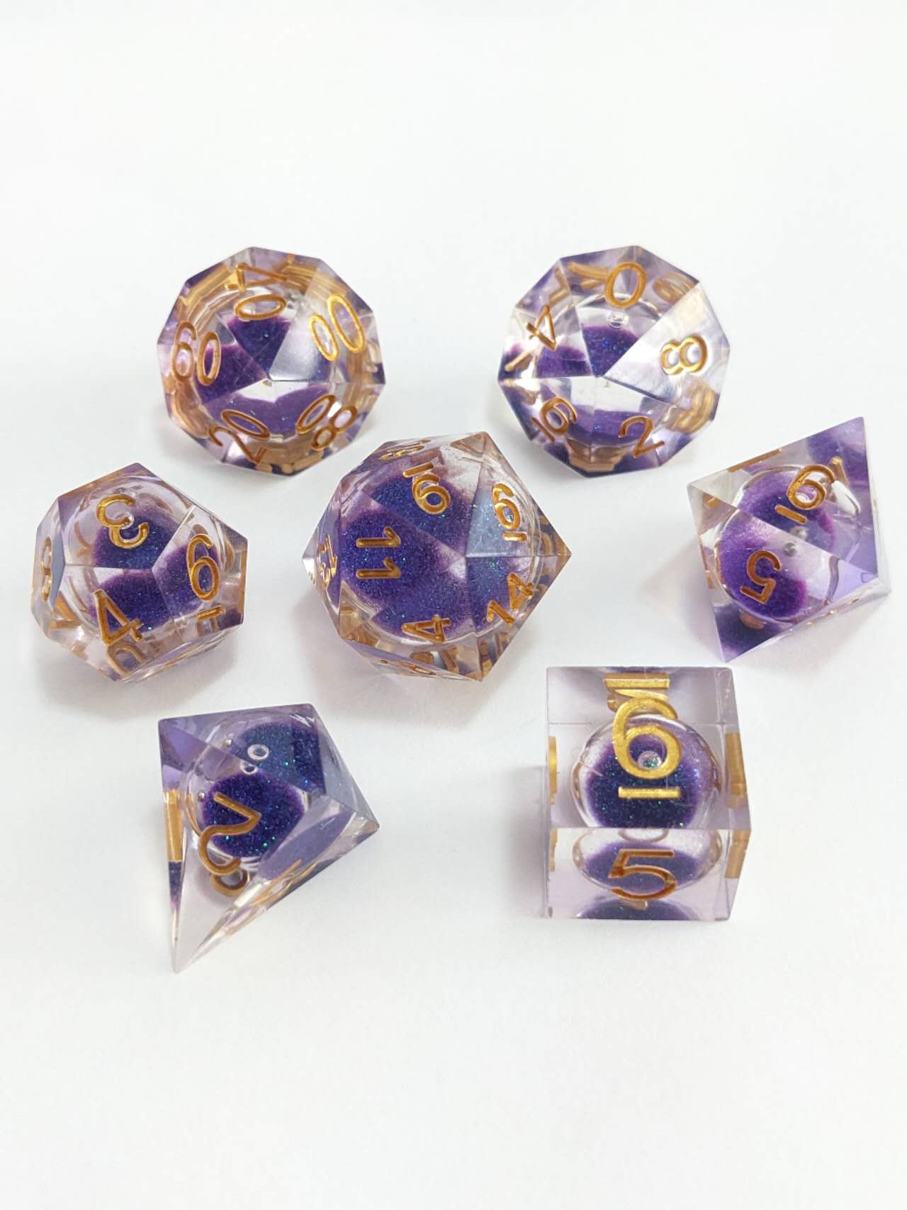 Seven clear resin polyhedral dice with purple glitter cores and gold numbers on a white background