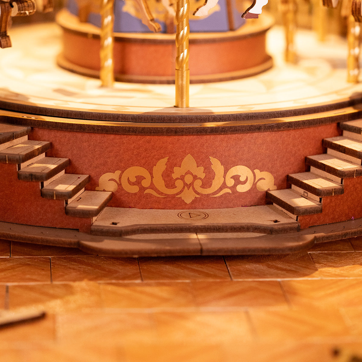 Close-up of an ornate wooden carousel music box base with gold patterns and small stairs