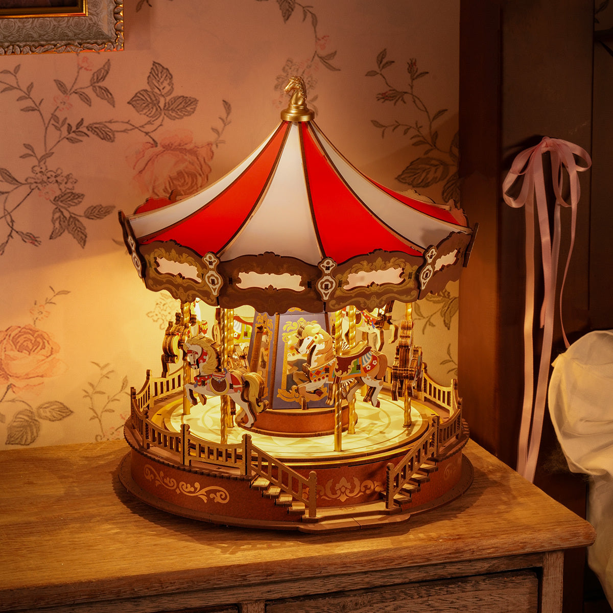 A miniature wooden carousel with a red and white striped roof and horses, glowing warmly on a wooden table