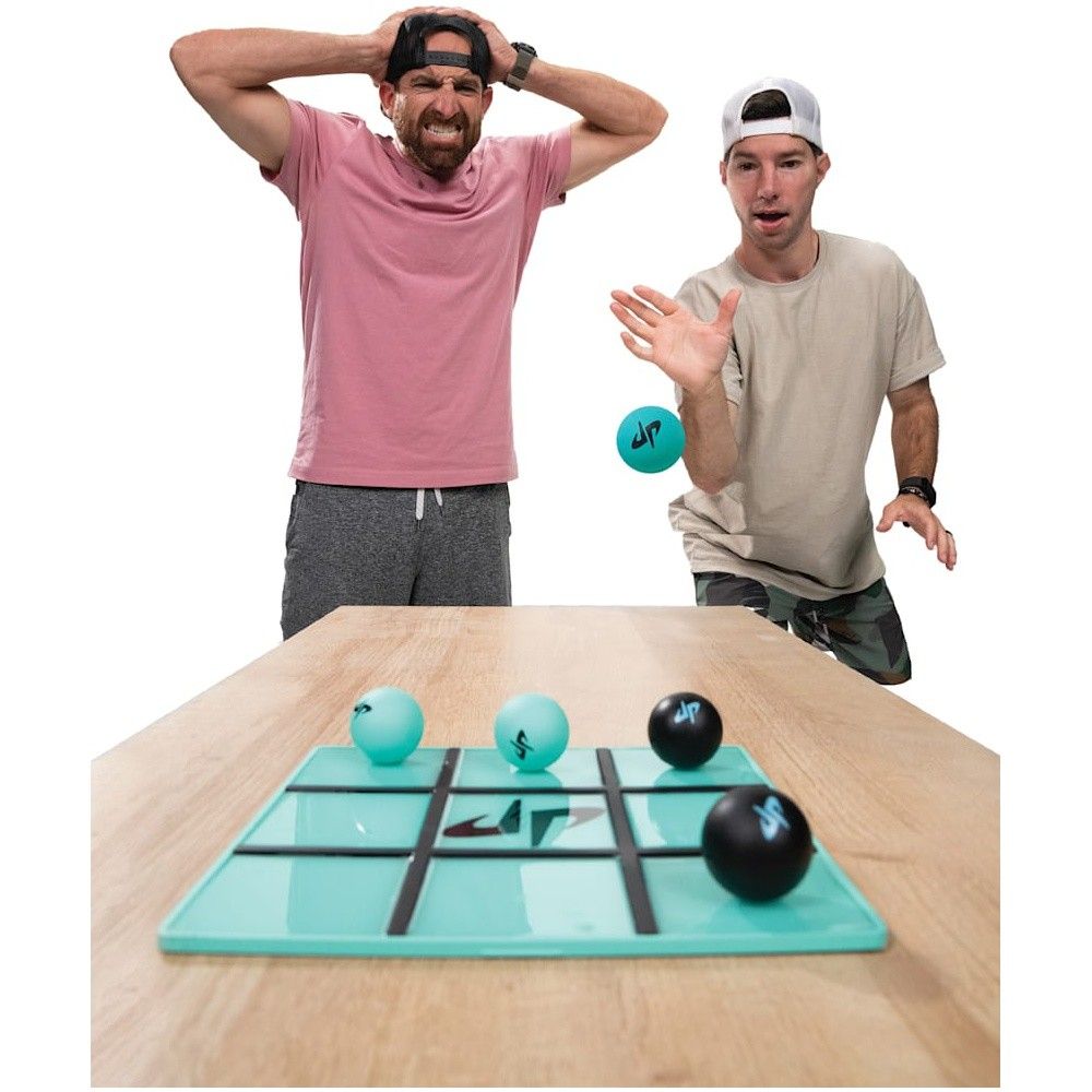 Two men play a ball-toss game on a tic-tac-toe board; one throws a turquoise ball, the other, frustrated, holds his head