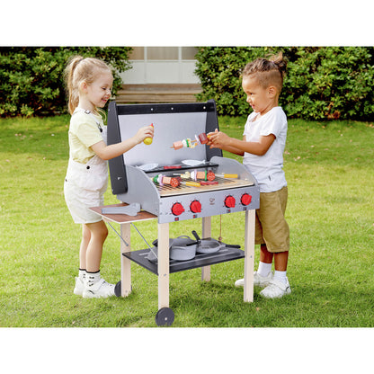 Two children grilling wooden play food skewers and sausages on a toy BBQ set outdoors