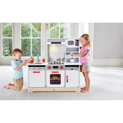 Two children playing with a modern Hape wooden play kitchen, featuring an oven, microwave, and sink