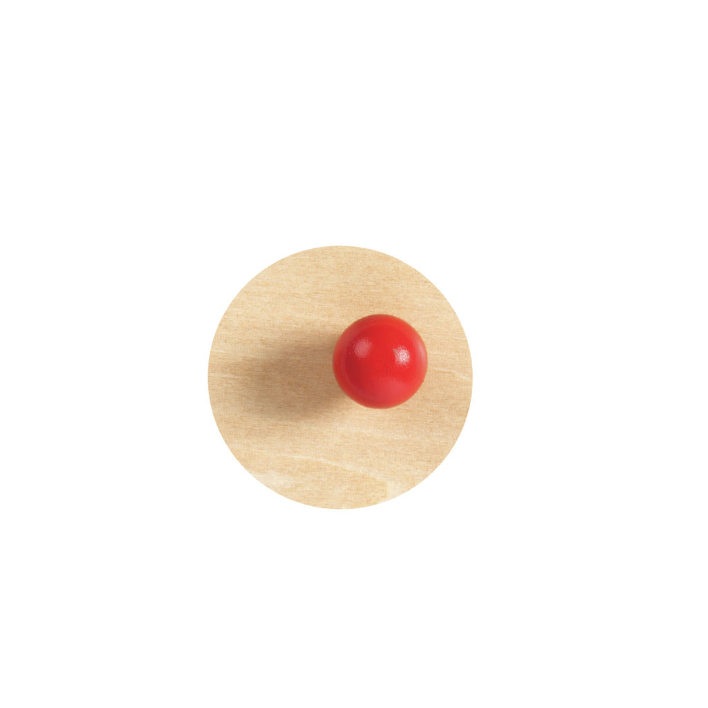 Wooden circle puzzle piece with a small, shiny red ball handle on a white background