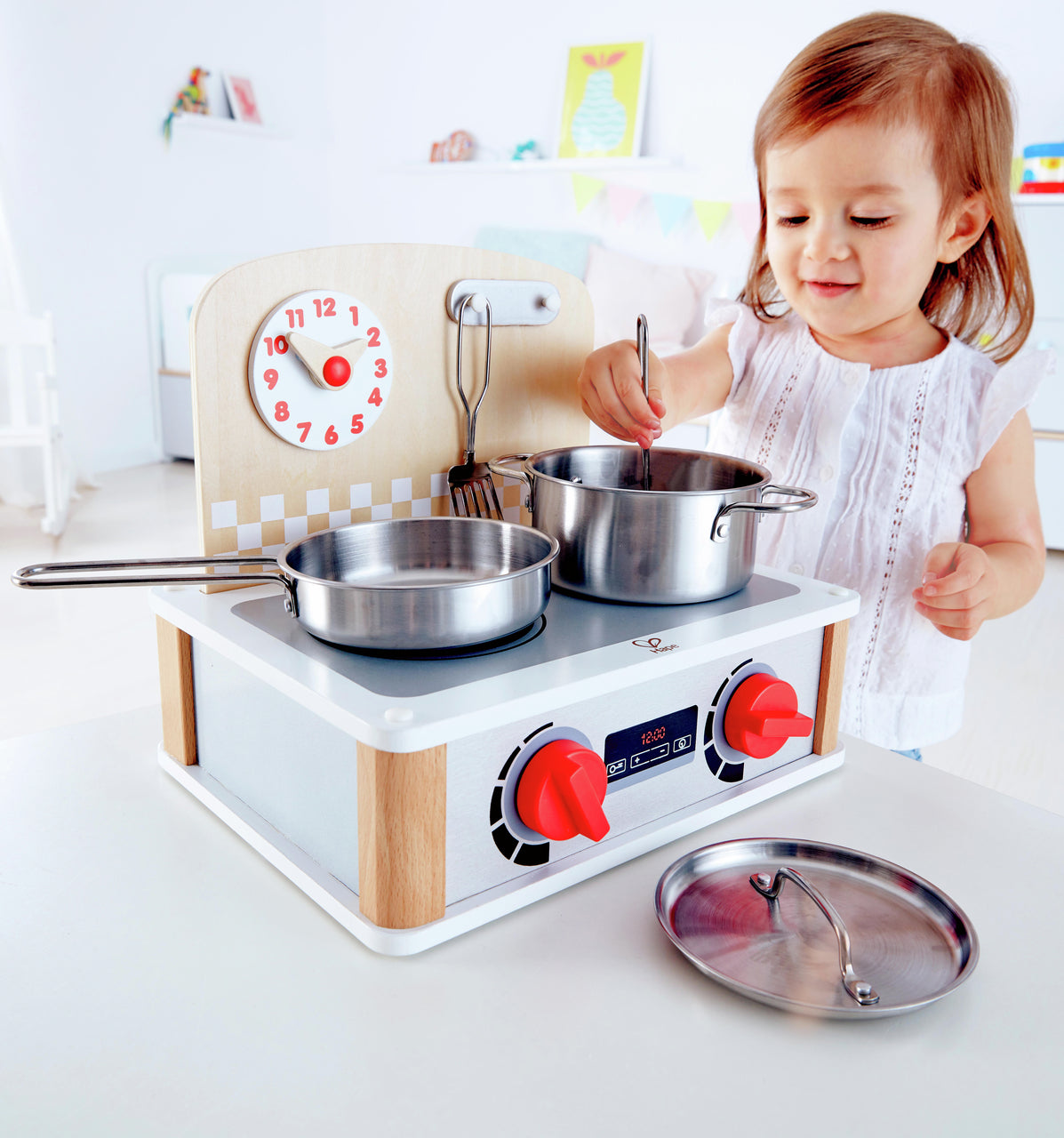 Toddler playing with a wooden play kitchen stove, stirring a realistic metal pot and pan