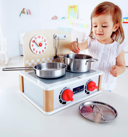 Toddler playing with a wooden play kitchen stove, stirring a realistic metal pot and pan