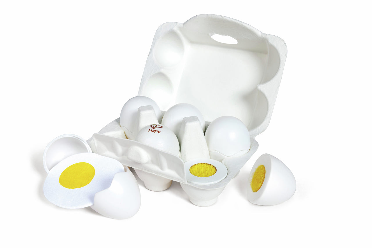 Six white play eggs in a carton; some are split open to show hard-boiled yellow yolks