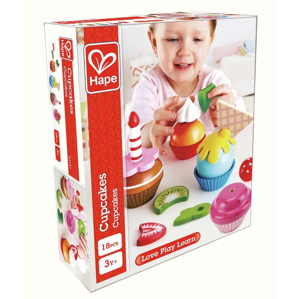 Smiling toddler playing with colorful toy cupcakes and wooden toppings on the Hape product box