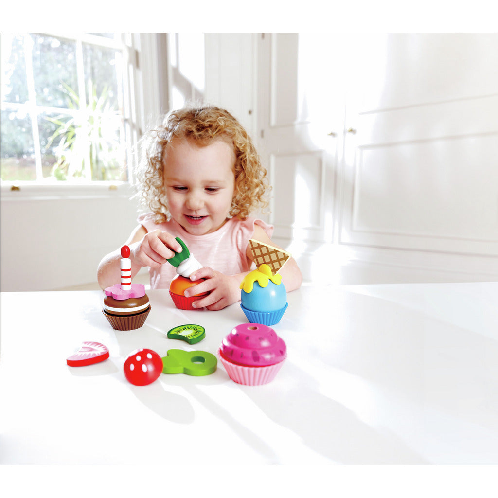 Smiling girl decorating colorful toy cupcakes with a green icing bottle
