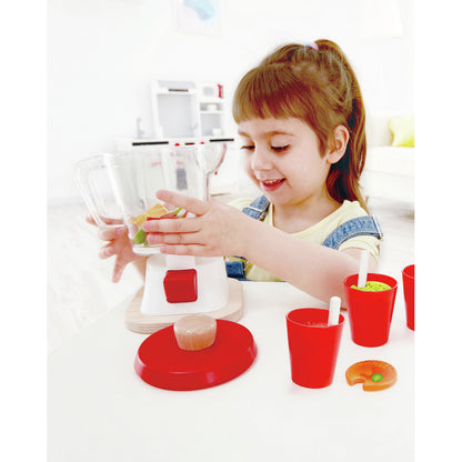 Smiling young girl plays with a toy smoothie blender, adding colorful fruit pieces