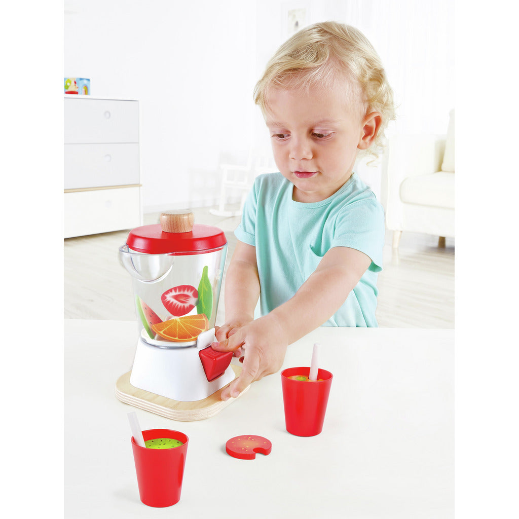 Toddler playing with a toy blender filled with wooden fruit slices, pressing the switch