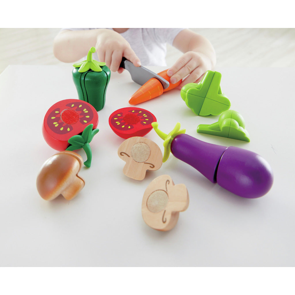 Child playing with colorful wooden vegetables, cutting a carrot with a toy knife