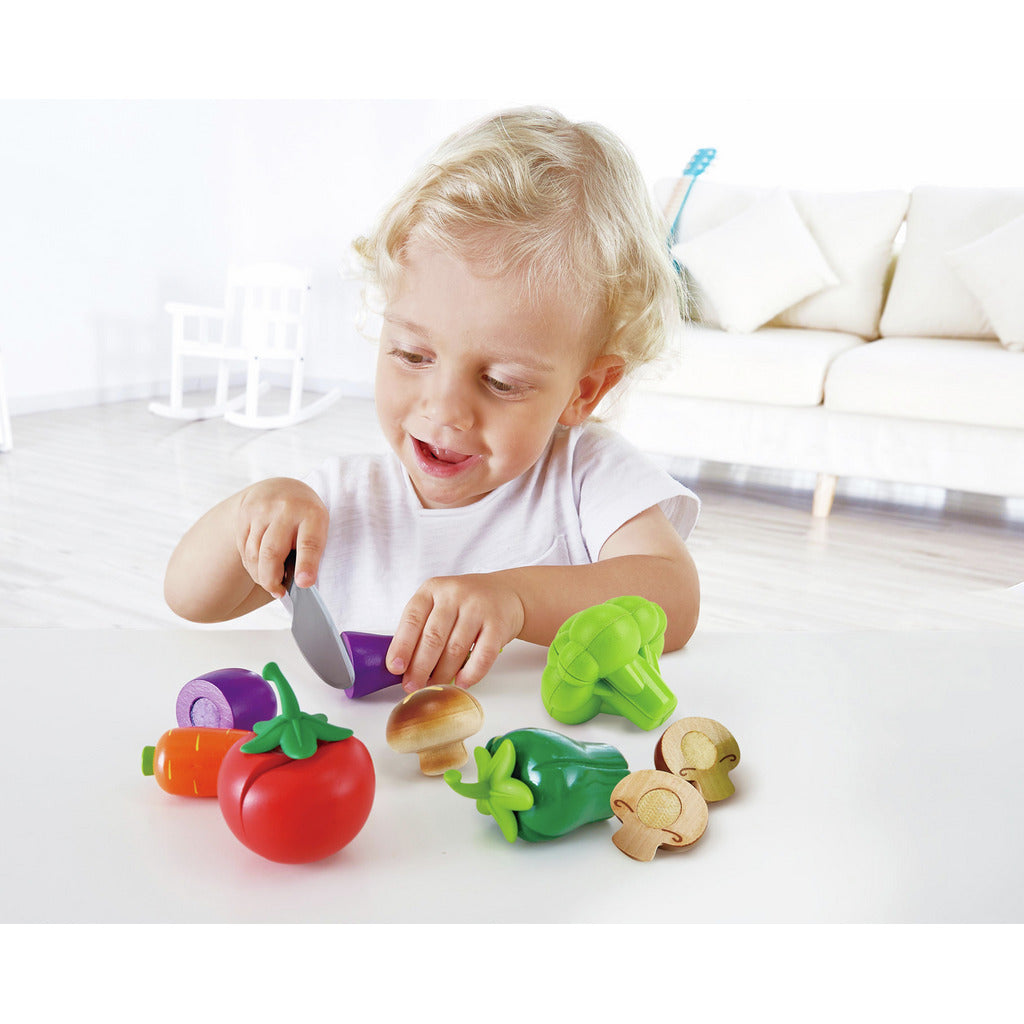 Happy toddler cutting colorful play food vegetables with a toy knife