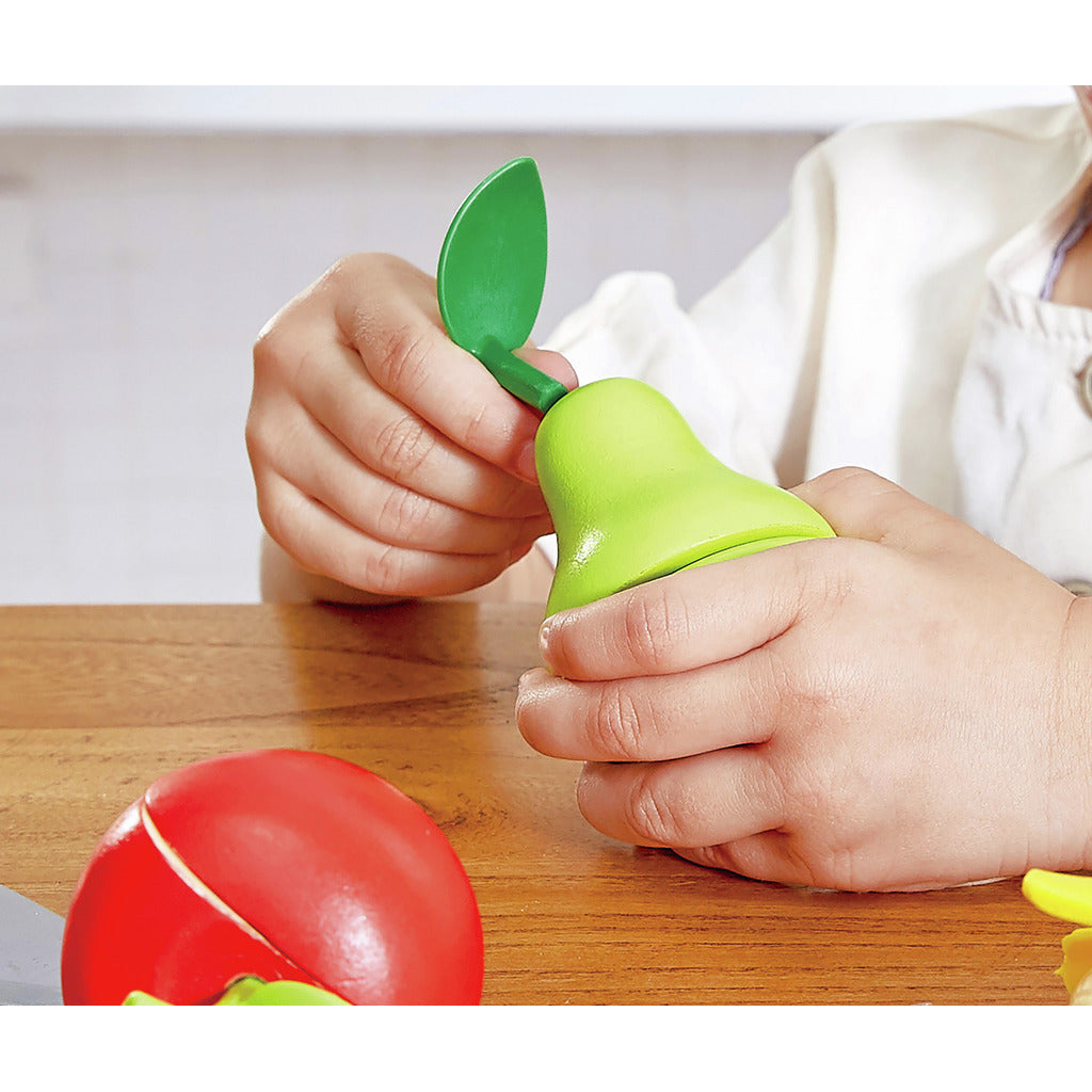 Child playing with wooden food, assembling the stem into a green toy pear