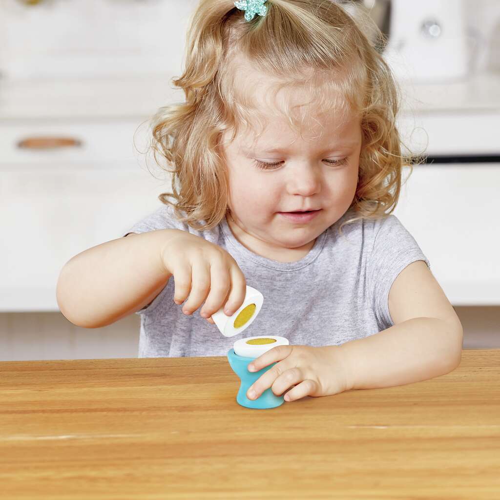 A young toddler intently plays with a toy half-egg, placing it into a small blue egg cup