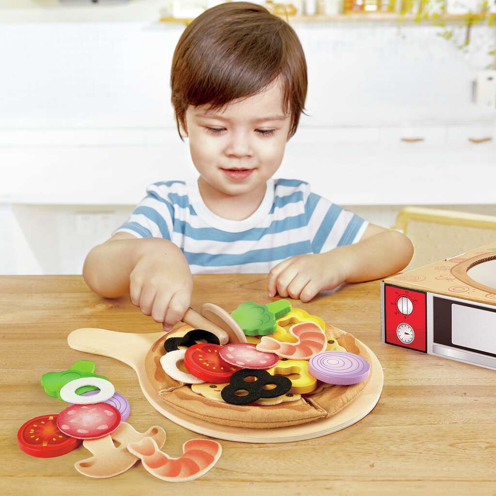 Young child playing with a wooden toy pizza set, arranging colorful toppings on a wooden peel