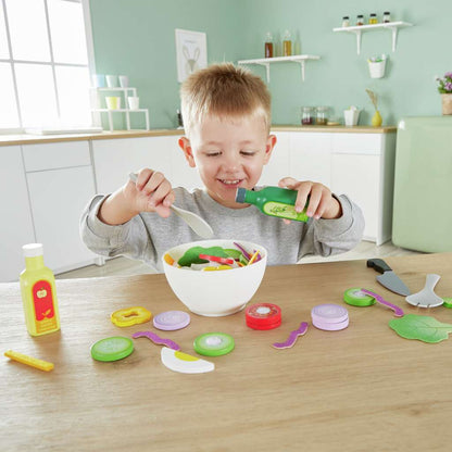 Smiling boy dressing a toy salad bowl with a play dressing bottle and spoon