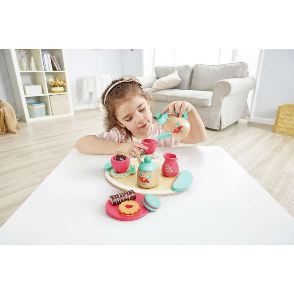 Child pouring tea from a bird-themed wooden teapot, playing with a colorful toy tea set and wooden treats