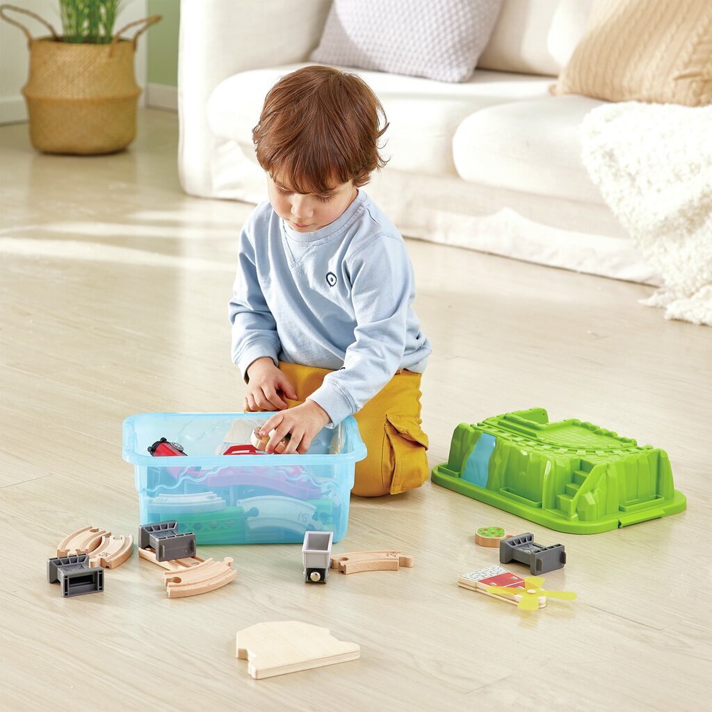 Toddler kneeling on a wooden floor, pulling wooden train tracks from a blue storage container