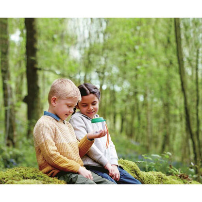 Two children in a forest happily examining a bug in a plastic observation jar